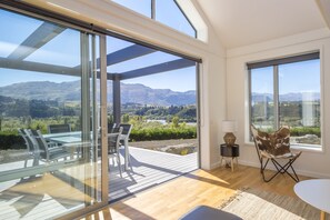 Un intérieur moderne avec une porte vitrée donnant sur une terrasse extérieure, un coin repas et une vue sur les montagnes.