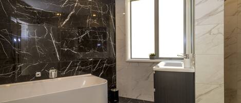 A modern bathroom with a freestanding bathtub, a window, and a sink.