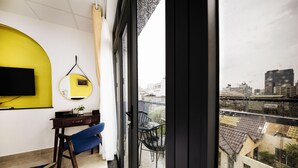 A hotel room with a bed, a desk, a chair, a TV, a mirror, and a window with a city view. - Chez Mimosa Petite (Ho Chi Minh City)