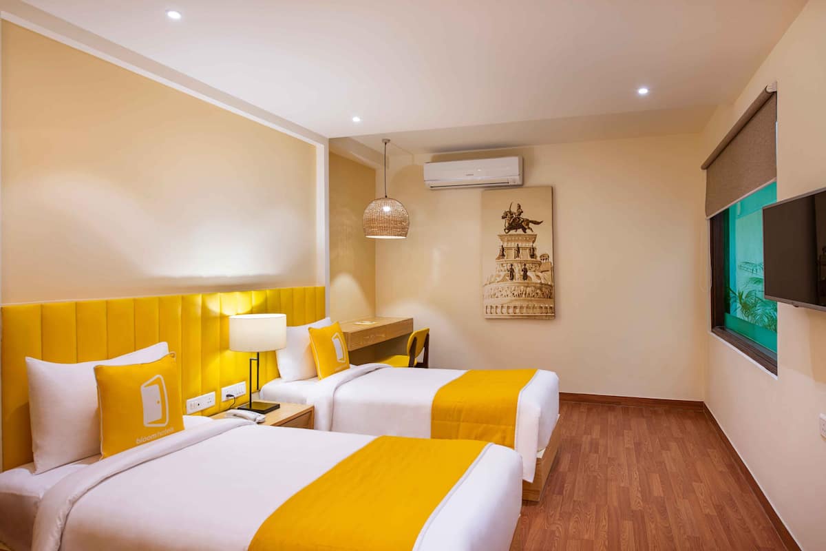 Una habitación de hotel con dos camas, un escritorio, una silla, un televisor y aire acondicionado.