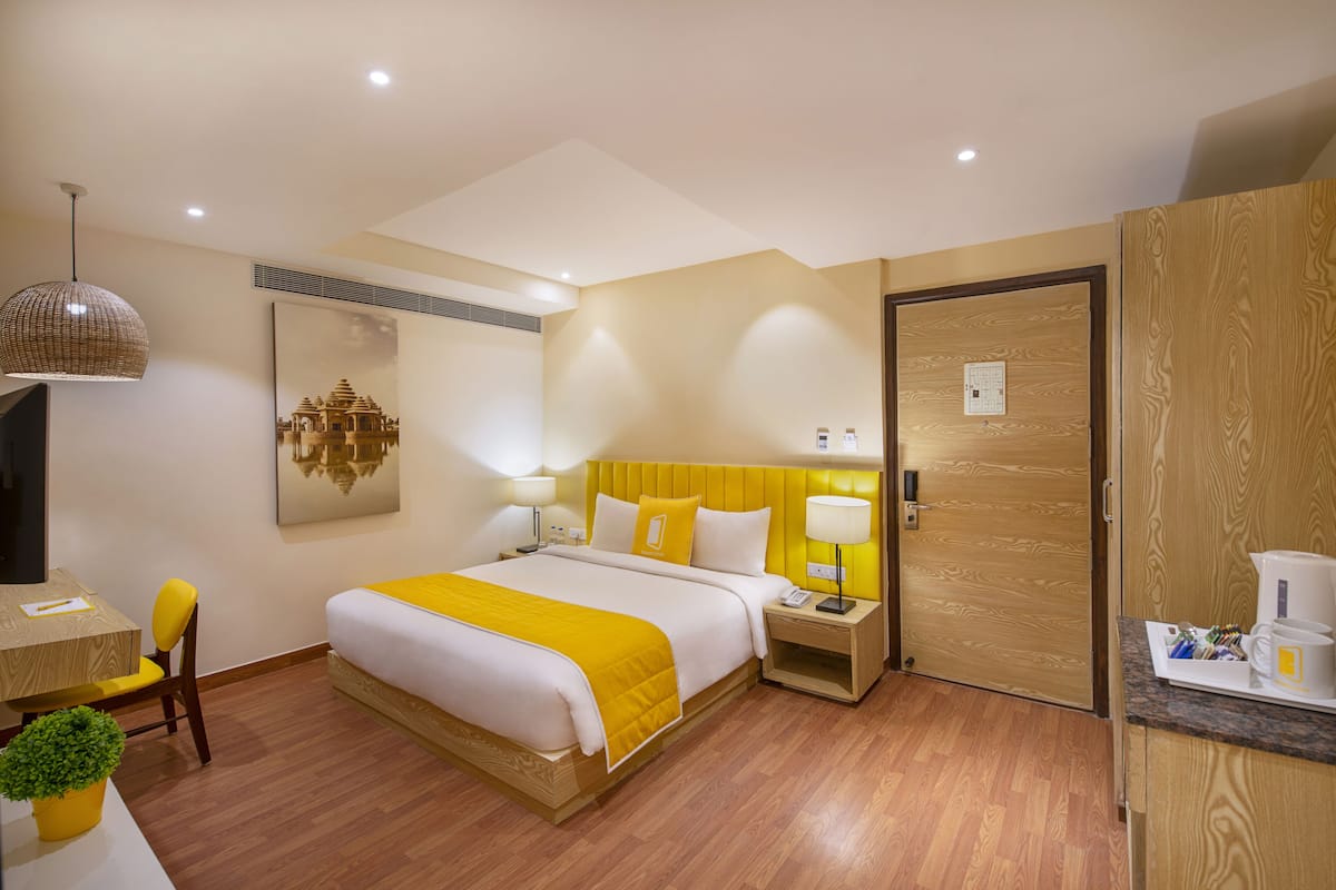 Habitación de hotel con cama, mesitas de noche, un escritorio, una silla, una planta en maceta y una puerta.