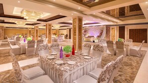 Un salón de banquetes con mesas redondas, sillas blancas y un fondo decorativo.