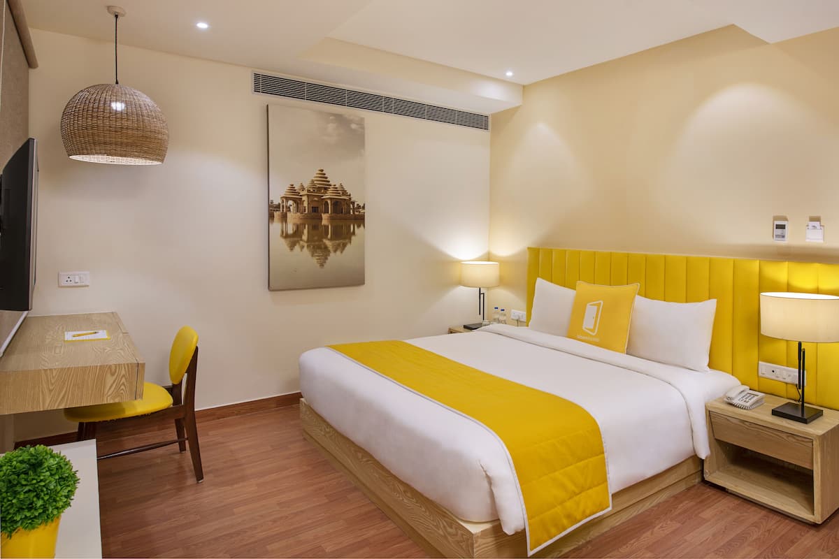 Habitación de hotel con cama, mesita de noche, lámpara y una obra de arte colgada en la pared.