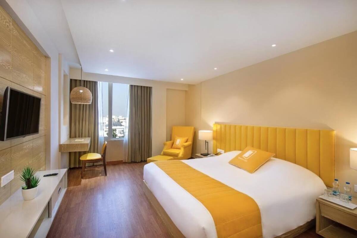 Una habitación de hotel con cama, escritorio, silla, televisor y ventana con cortinas.