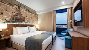 Habitación de hotel con una cama grande, un escritorio con lámpara, televisión y vistas a la ciudad.