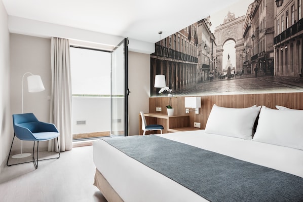 A hotel room with a large bed, a desk, a chair, a lamp, and a view of a historic archway.