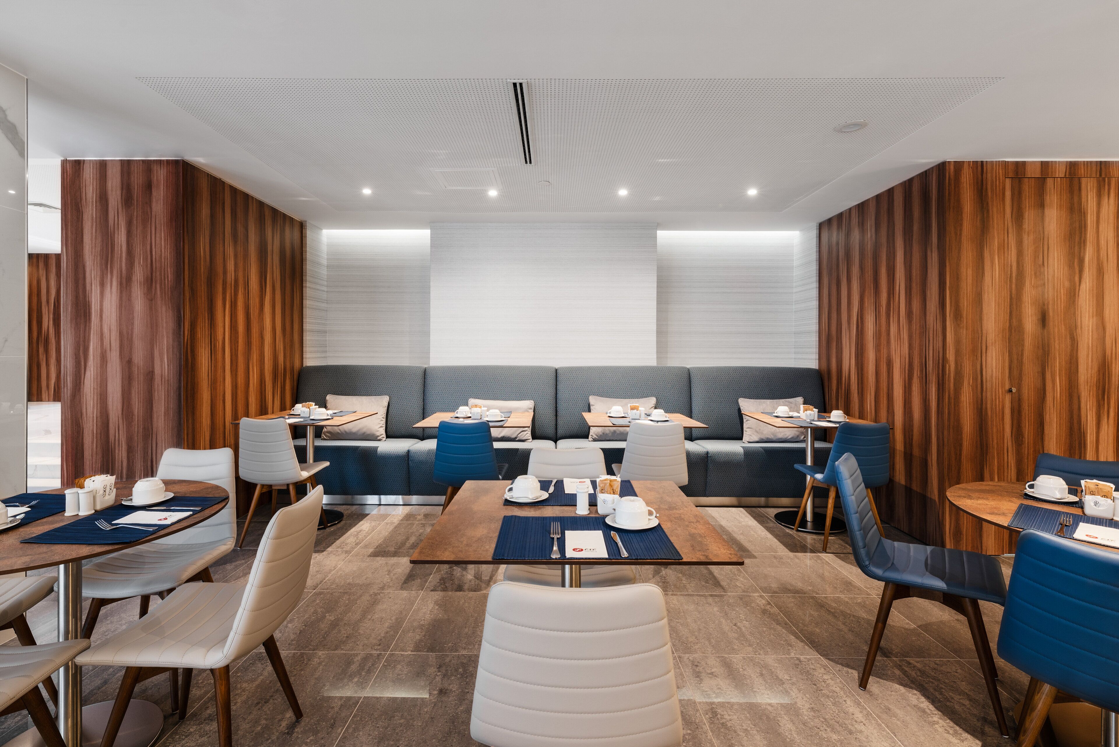 Un espace de restauration moderne avec des murs recouverts de panneaux en bois, un coin salon central et des tables dressées pour le repas.