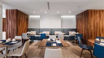 Un espace de restauration moderne avec des murs recouverts de panneaux en bois, un coin salon central et des tables dressées pour le repas.