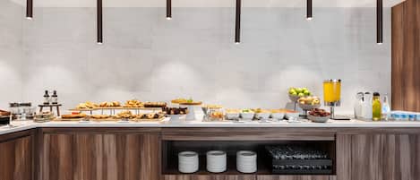 Una barra de desayuno moderna con una variedad de alimentos, como pasteles, frutas y bebidas.