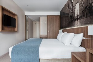 A modern hotel room with a large bed, a mounted TV, and a cityscape mural on the wall.