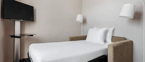 Habitación de hotel ordenada con cama, televisor en un soporte, lámpara de pared y una mesita.