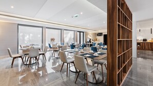 Un salón de conferencias moderno con mesas redondas, sillas y una estantería de madera.
