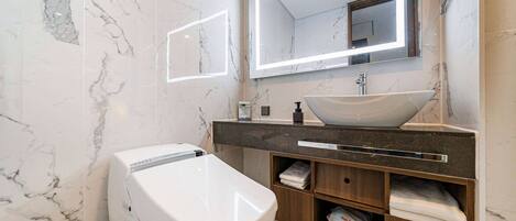 A modern bathroom with a marble floor, a white toilet, a vanity with a sink, and a large mirror with a light strip.