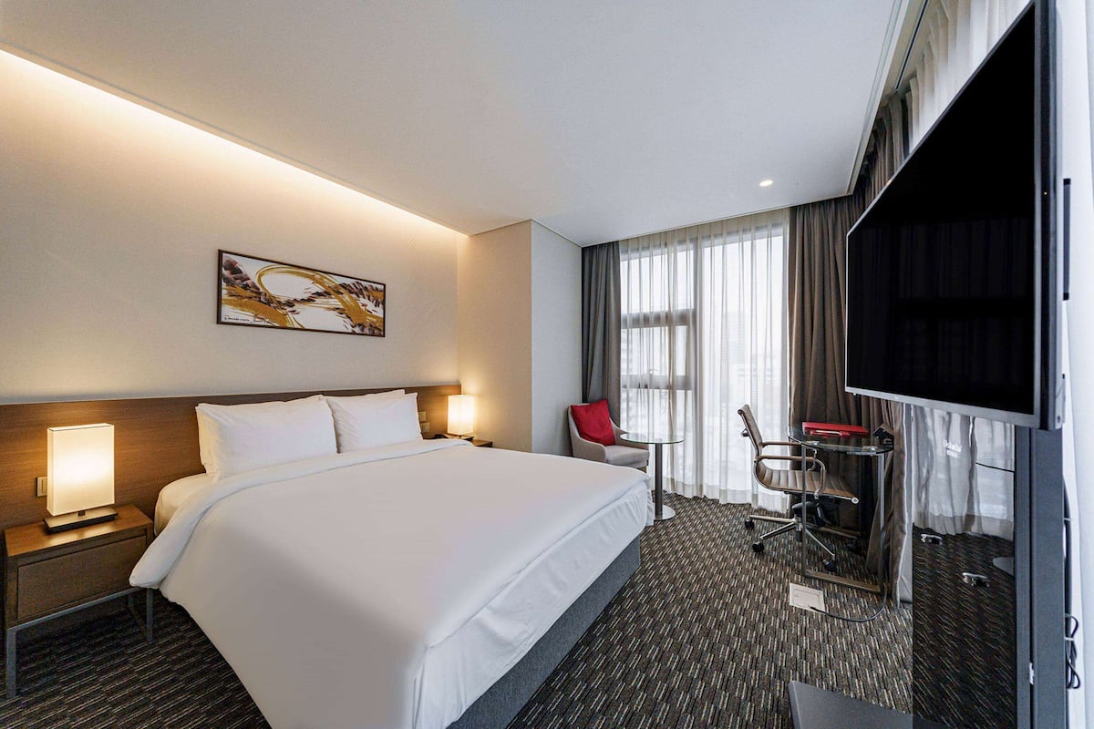 Habitación de hotel con una cama grande, un escritorio con silla, televisión y un cuadro en la pared.