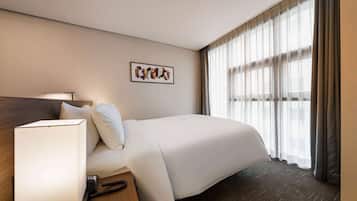 Una habitación de hotel con cama, mesita de noche, lámpara y ventana con cortinas.