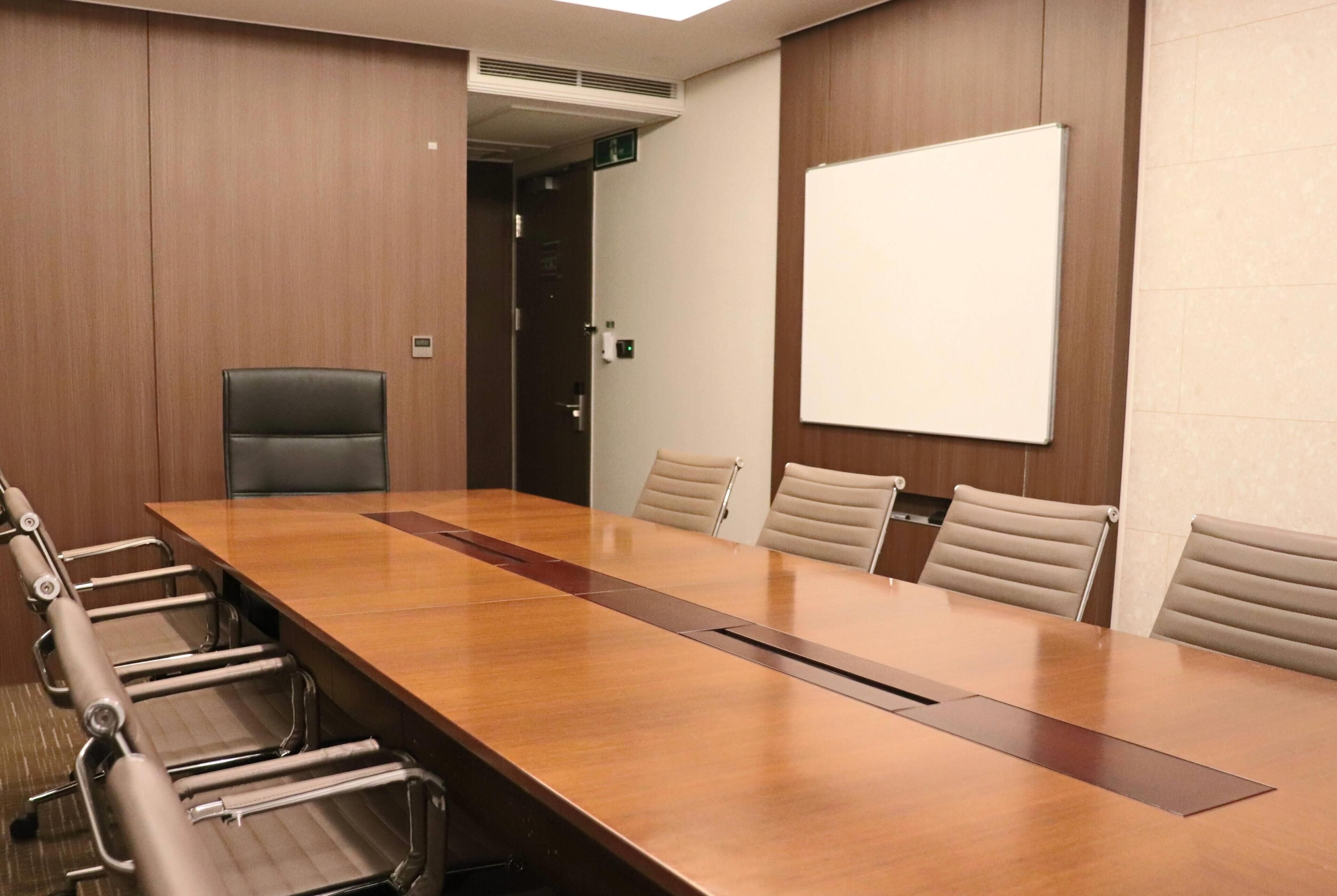 A conference room with a long wooden table, six chairs, and a whiteboard on the wall.