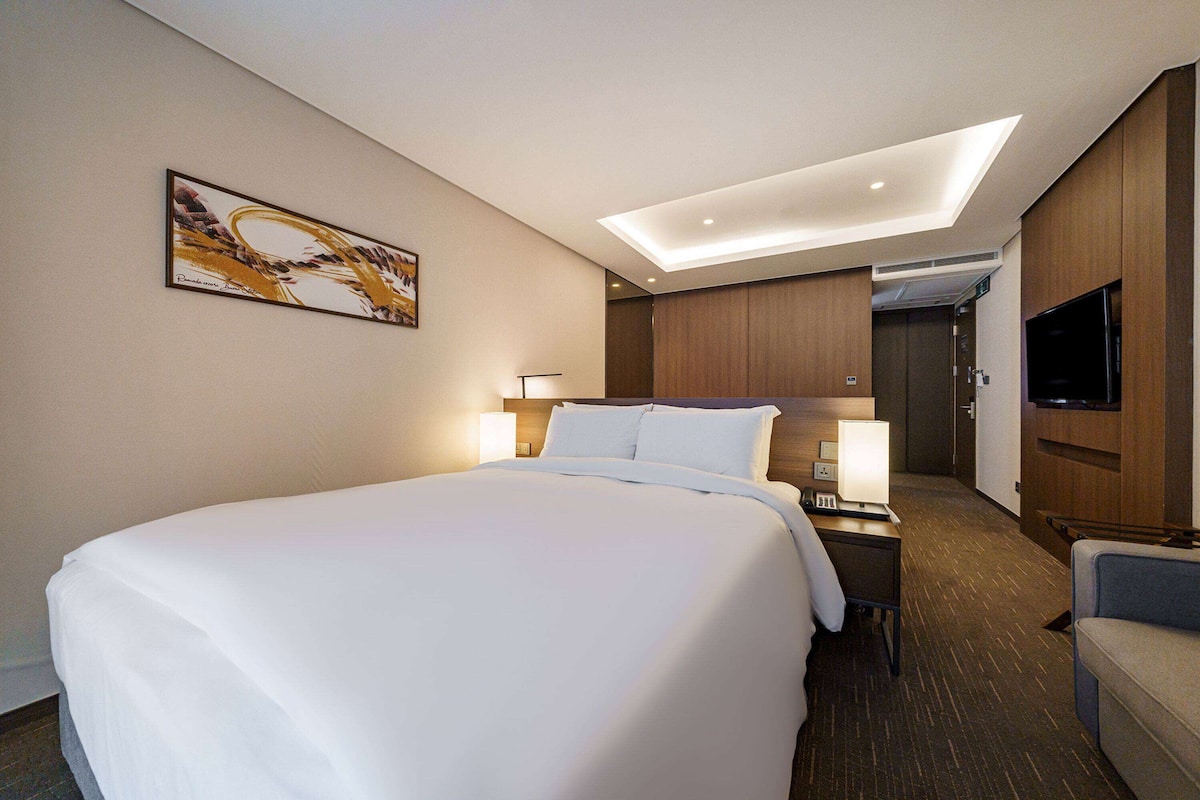 Habitación de hotel con una cama grande, un escritorio con lámpara, un televisor de pantalla plana y un cuadro en la pared.