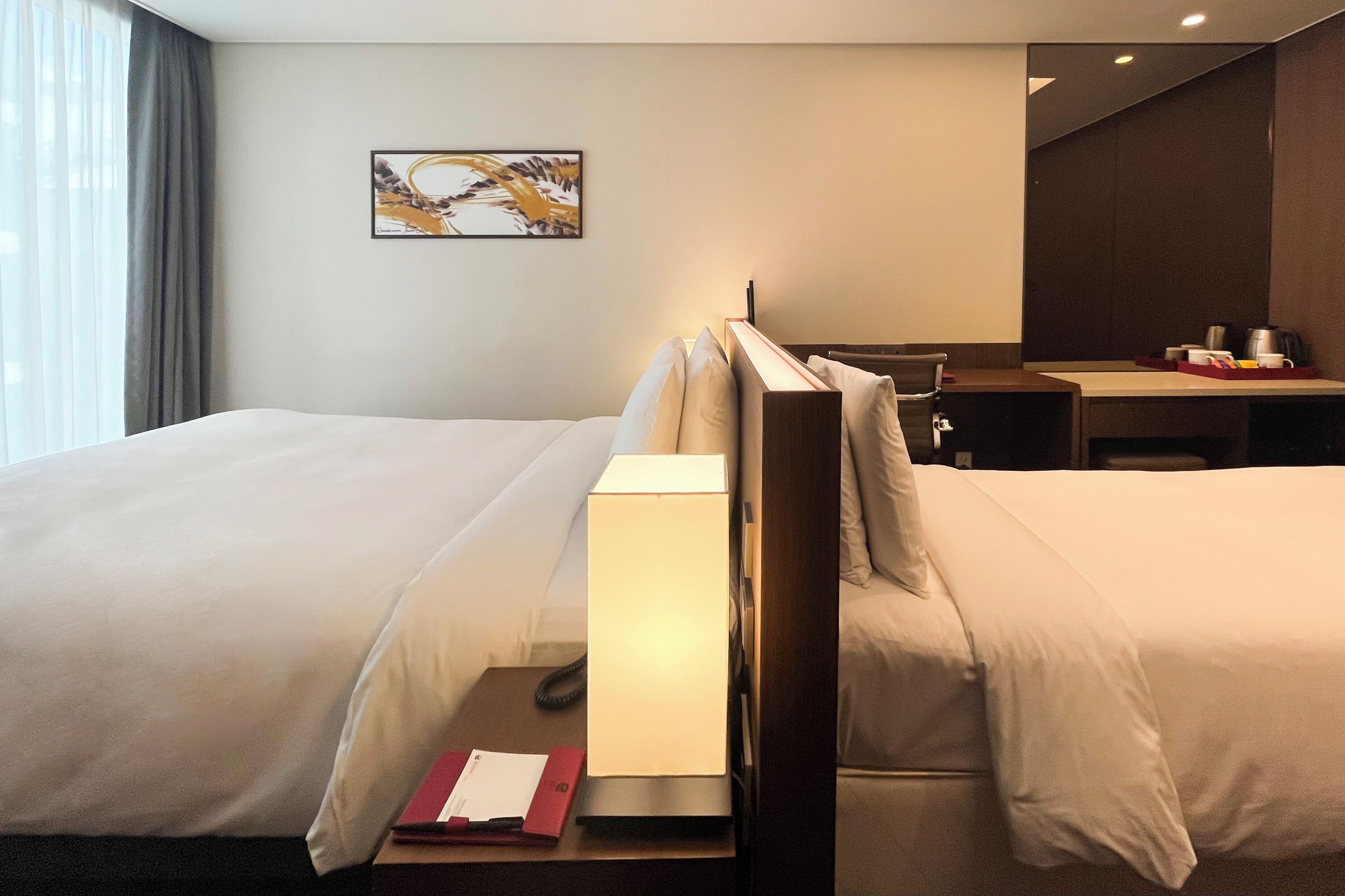 A hotel room with two beds, a desk, and a chair.
