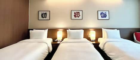 A hotel room with three single beds, each with a bedside table and lamp, and a wall with three framed artworks.