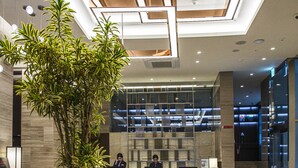 A modern reception area with a large potted plant, a red chair, and a reception desk. - Ramada Encore by Wyndham Busan Station (Busan)