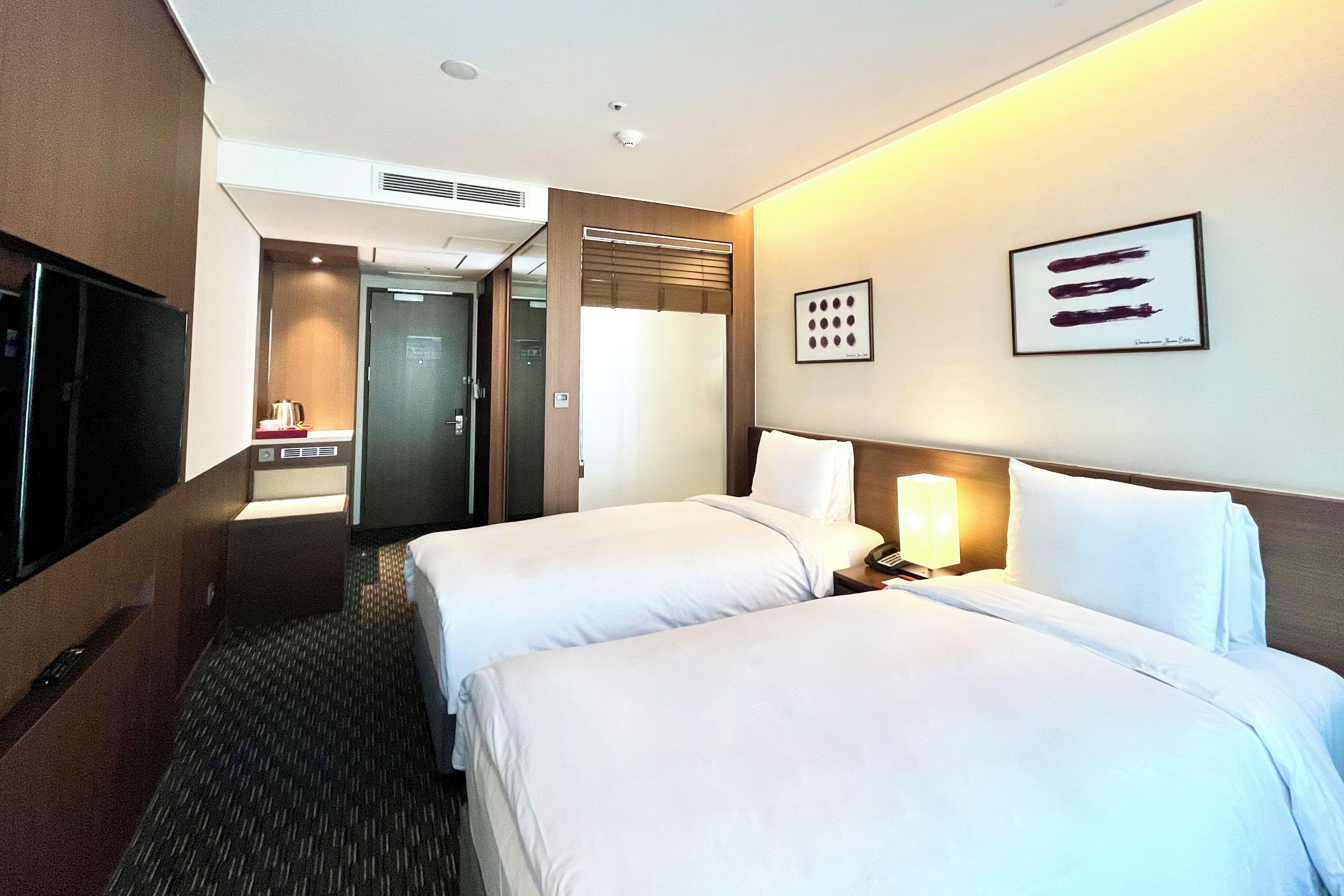 A hotel room with two beds, a TV, a bathroom, and a framed picture on the wall.