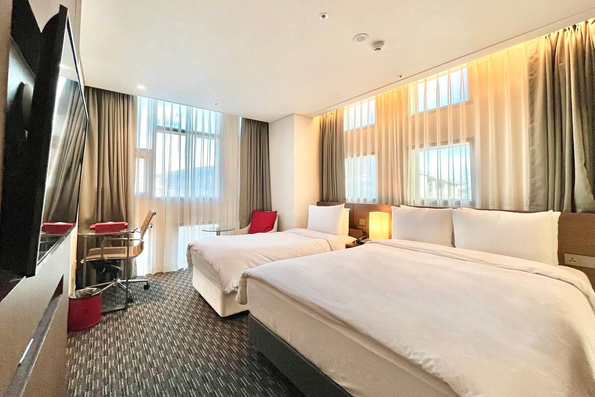 Habitación de hotel con dos camas, un escritorio, una silla y un televisor.