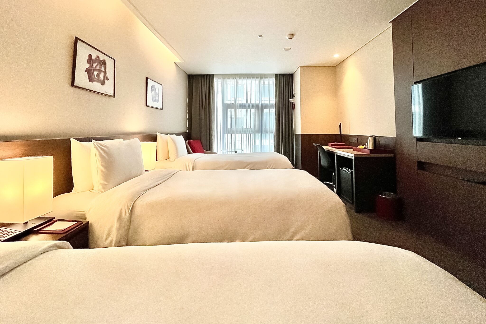 A hotel room with two beds, a desk, a TV, and a window with curtains.