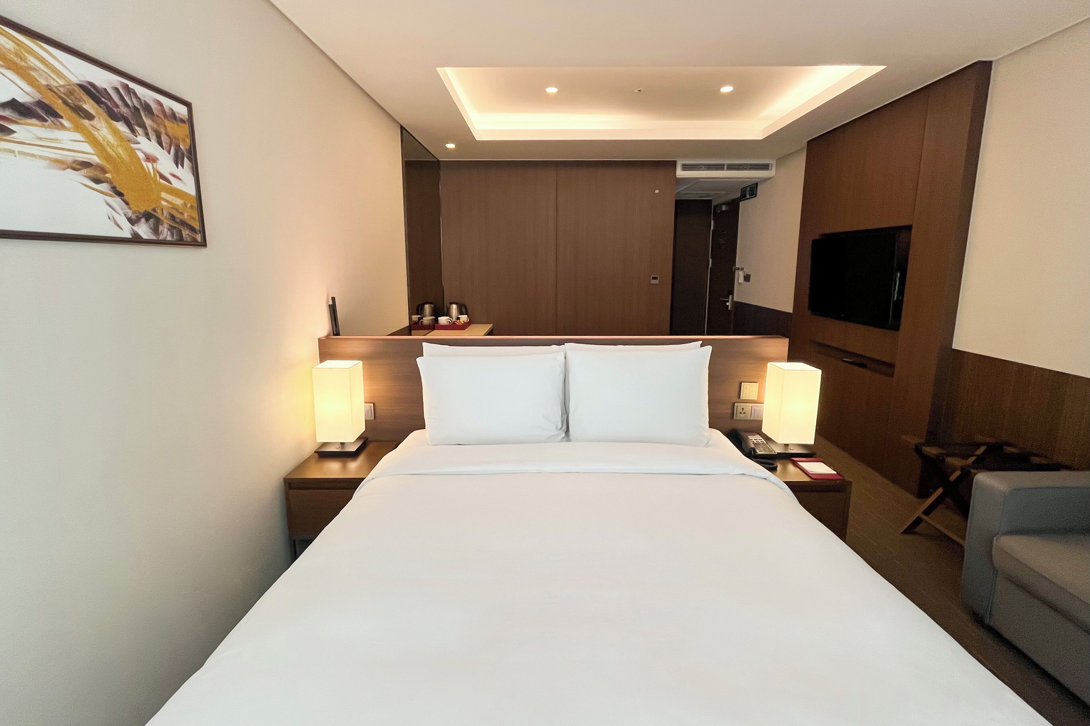 A hotel room with a large bed, bedside lamps, a flat-screen TV, and a wooden headboard.