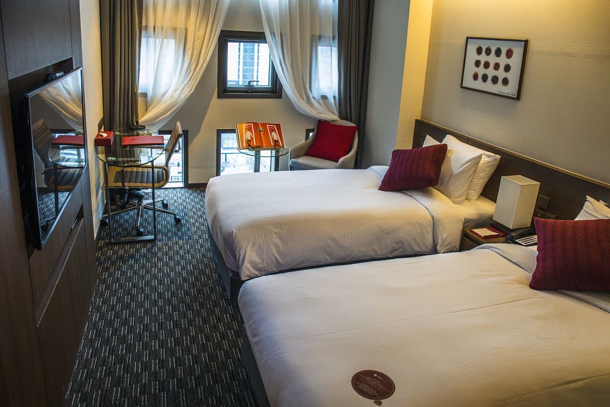 Habitación de hotel con dos camas, un escritorio, una silla, una mesita y una ventana con cortinas.