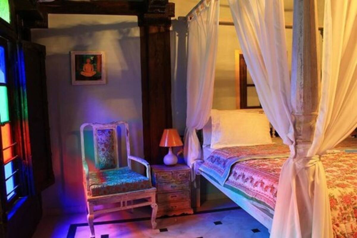 Une chambre avec un lit à baldaquin, une chaise, une table de chevet et un tableau accroché au mur.