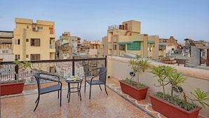Terraza en la azotea con dos sillas y una mesa, rodeada de plantas en macetas.