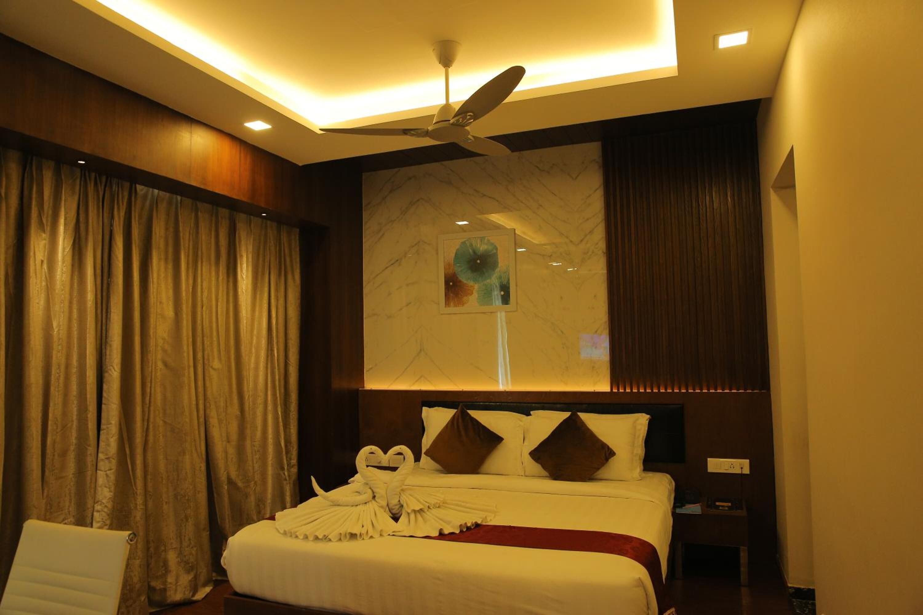 A hotel room with a bed, a ceiling fan, a large window with curtains, and a wall-mounted artwork.