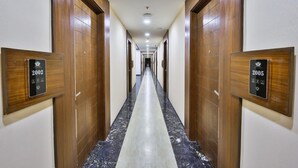 A hotel hallway with wooden doors, numbered room signs, and a marble floor. - The Royal Grand (Karur)