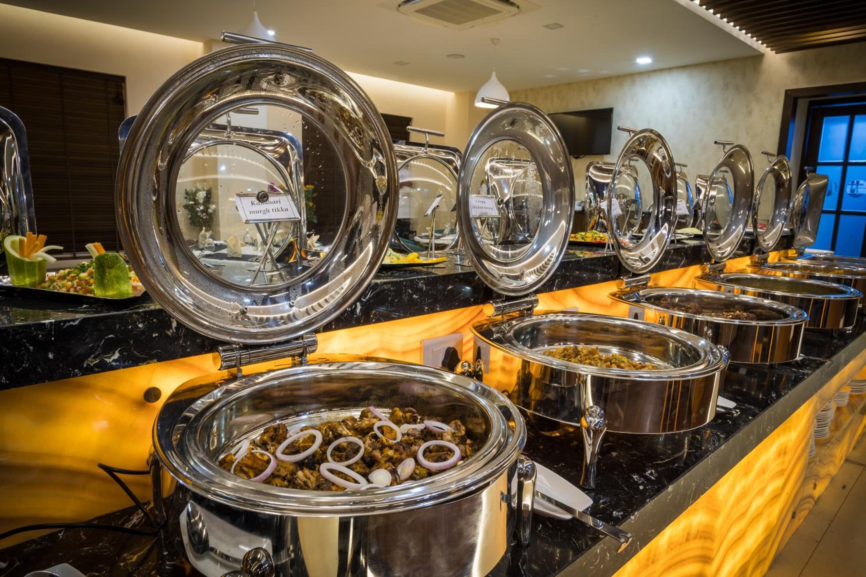 A buffet setup with multiple stainless steel chafing dishes and lids, arranged on a marble countertop.