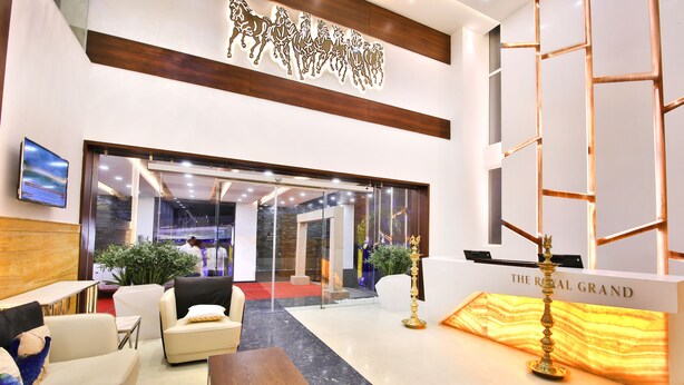 A hotel lobby with a reception desk, seating area, and a decorative wall with horse silhouettes. - The Royal Grand (Karur)