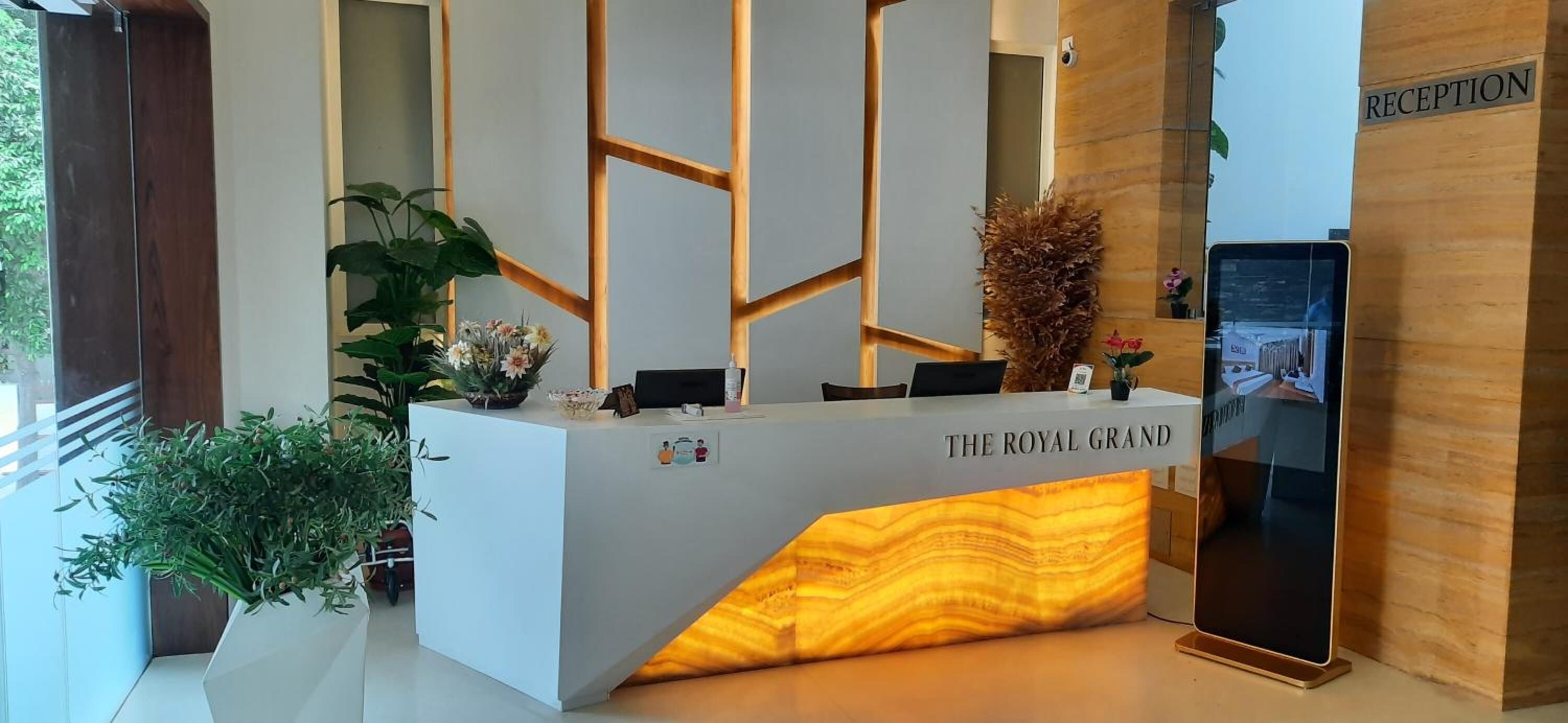 Un comptoir d’accueil portant l’inscription « The Royal Grand », doté d’un design moderne, avec des panneaux muraux aux motifs géométriques et un élément décoratif en bois.