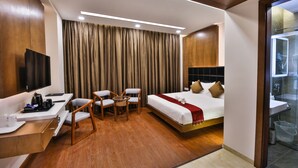 A hotel room with a bed, a desk with a chair, a television, and a shower area. - The Royal Grand (Karur)