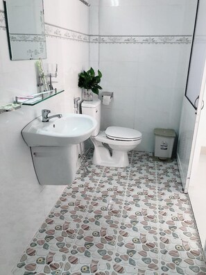 A small bathroom with a white sink, toilet, and a trash bin. There is a mirror on the wall and a plant on the sink. - Moonlight Home (Ho Chi Minh City)