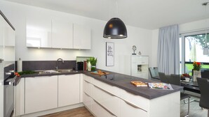 A modern kitchen with white cabinets, a black pendant light, and a dining area with a table and chairs.