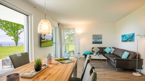A modern living room with a wooden dining table, a sofa, and a large window offering a view of the outdoors.