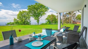 An outdoor dining area with a table set for two, overlooking a grassy lawn and a body of water.