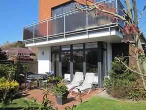 Una casa moderna con balcón de cristal, mobiliario exterior y jardín.