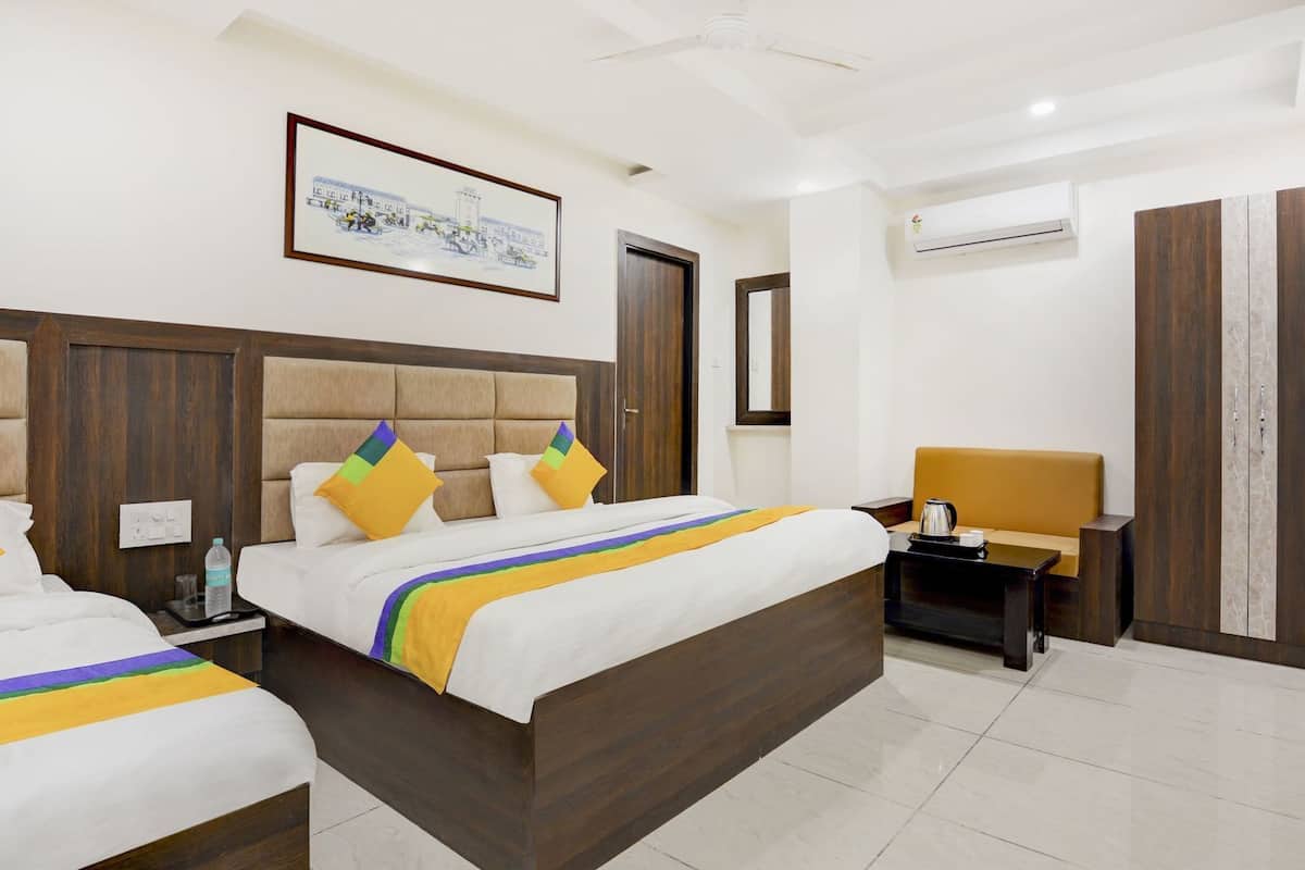 A hotel room with two beds, a ceiling fan, an air conditioning unit, a framed picture on the wall, and a nightstand with a kettle.