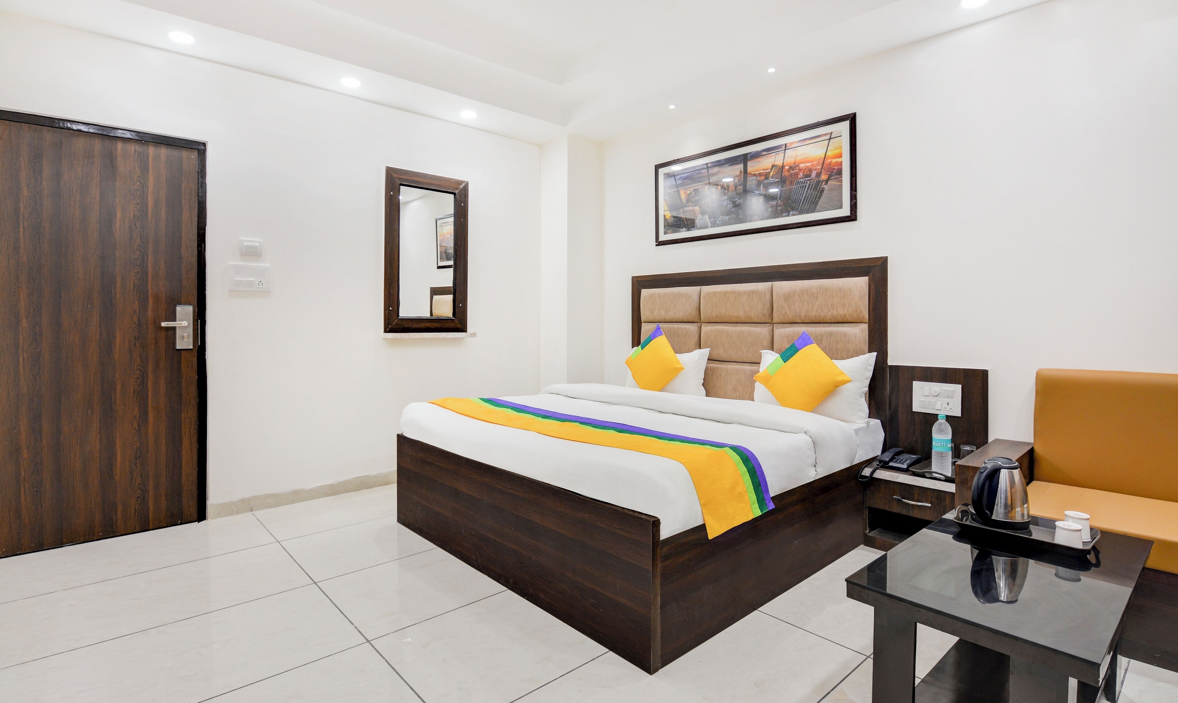 Una habitación de hotel con una cama de madera, una mesita de noche con una tetera y una silla.
