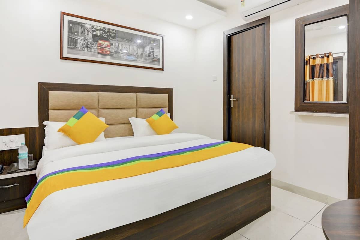 A neatly arranged hotel room with a bed, a bedside table, a nightstand, a mirror, and a door.