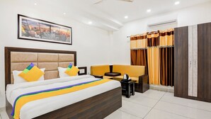 A hotel room with a large bed, a sofa, a small table, and a wardrobe. - Itsy Hotels K K Residency Staywell (Roorkee)