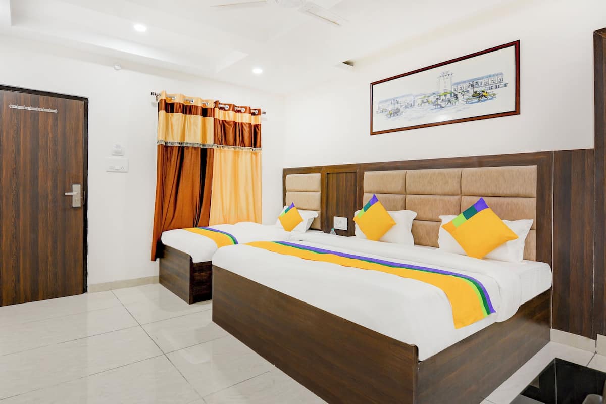 A hotel room with a large bed, two bedside tables, a wooden headboard, a framed picture on the wall, and a door.