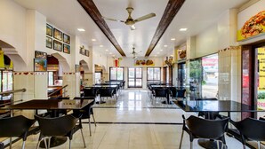 A spacious restaurant with high ceilings, ceiling fans, and a central aisle leading to the back. Tables and chairs are arranged for dining. - Treebo Garden Cottage & Lawn Mahabaleshwar (Mahabaleshwar)