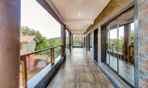 A corridor with a wooden floor, glass doors, and a view of greenery outside. - Treebo Garden Cottage & Lawn Mahabaleshwar (Mahabaleshwar)