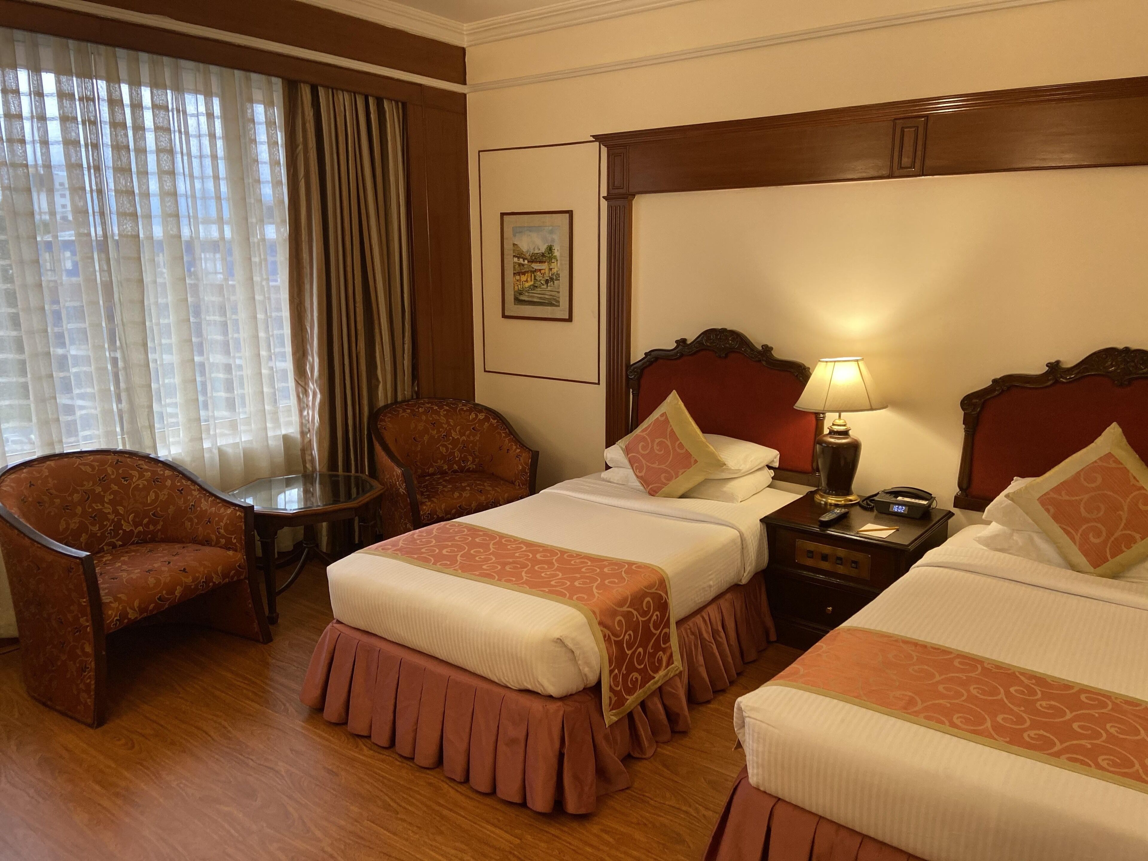 A hotel room with two beds, a chair, a small table, and a lamp.